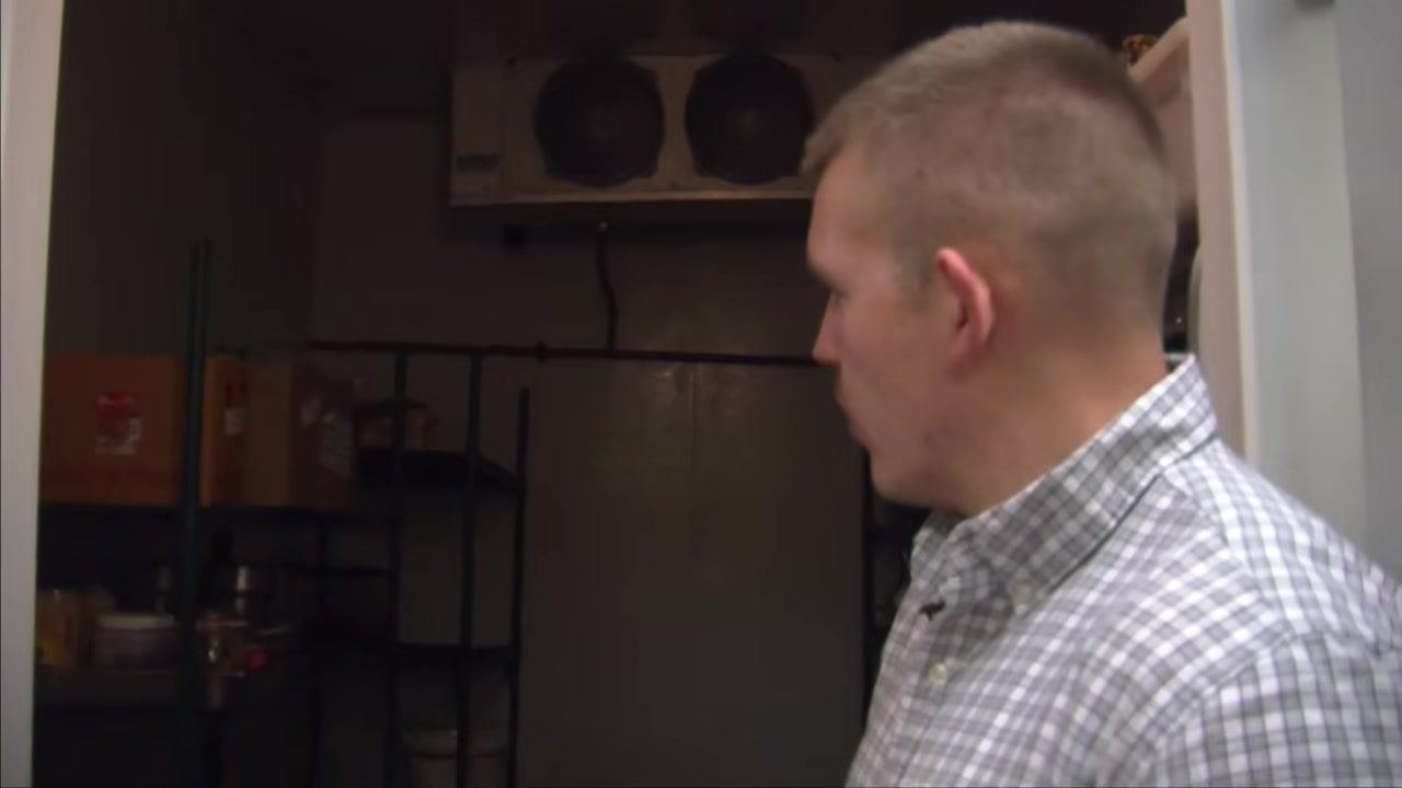 Close-up of metal shelving inside a walk-in refrigerator, holding various food containers and jars