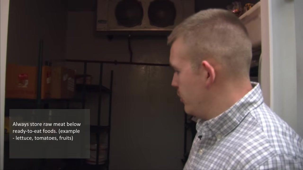 Person holding a thermometer in a commercial kitchen, explaining the temperature danger zone, with kitchen equipment and posted instructions in the background