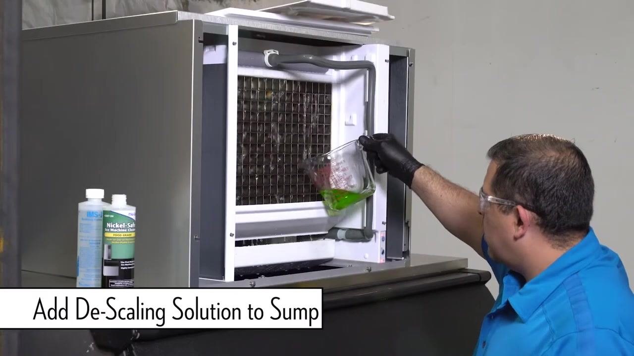 Technician in blue shirt and safety glasses facing the Ice-O-Matic machine, with bottles of IMS-II and Nickel-Safe cleaner visible nearby.