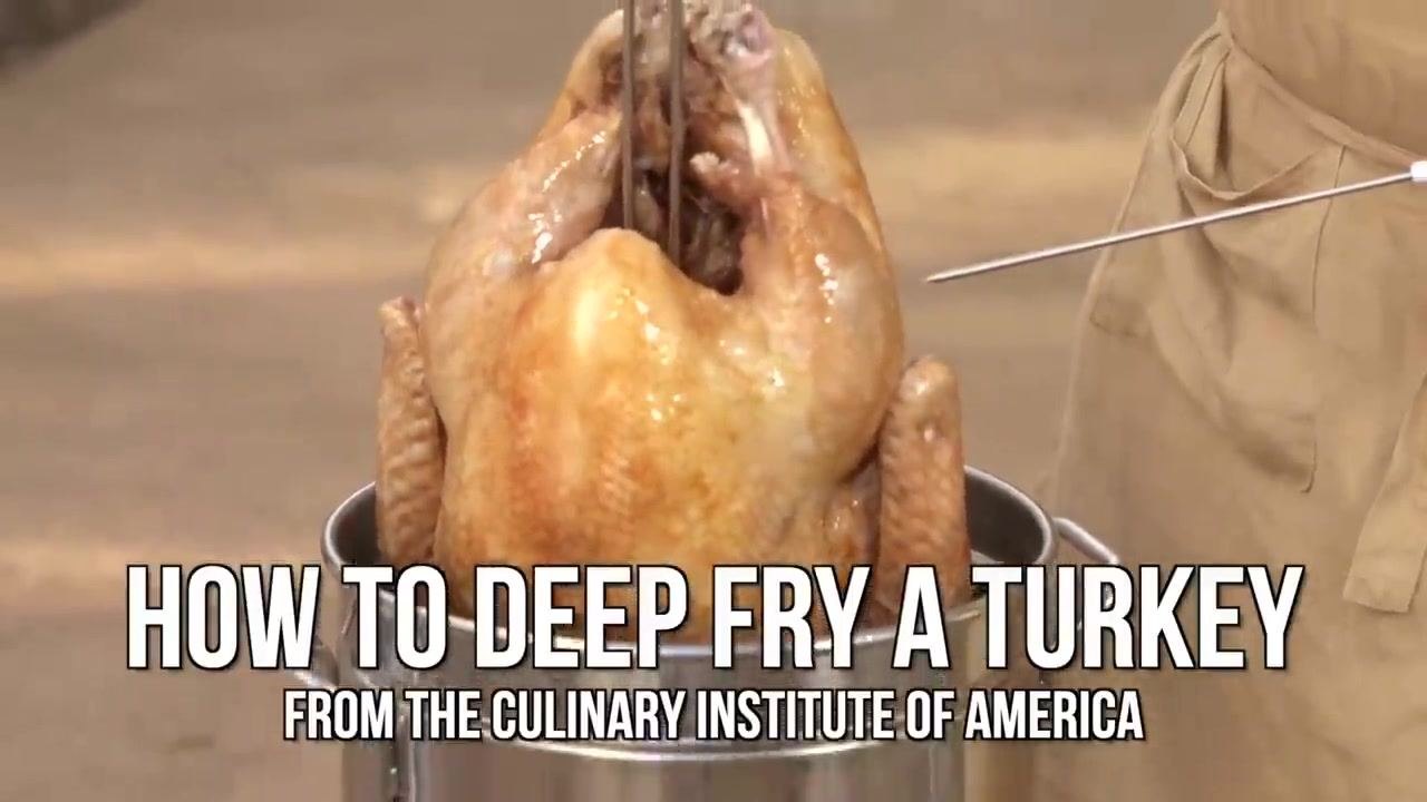 A whole cooked turkey being lifted from a fryer basket, with the text "HOW TO DEEP FRY A TURKEY FROM THE CULINARY INSTITUTE OF AMERICA" overlaid.