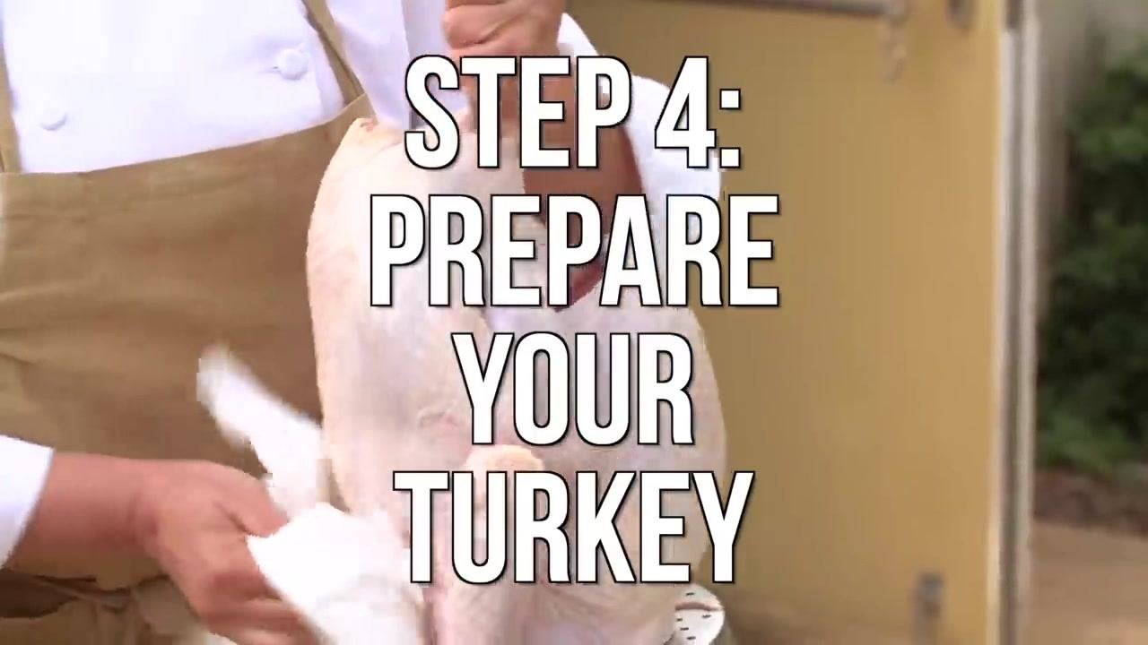 A person pats a raw turkey dry with paper towels.