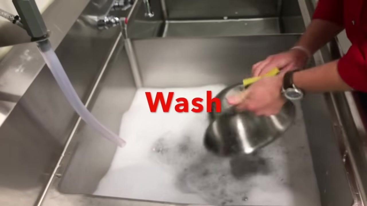 Staff member rinsing a metal pan in clear water using a sponge
