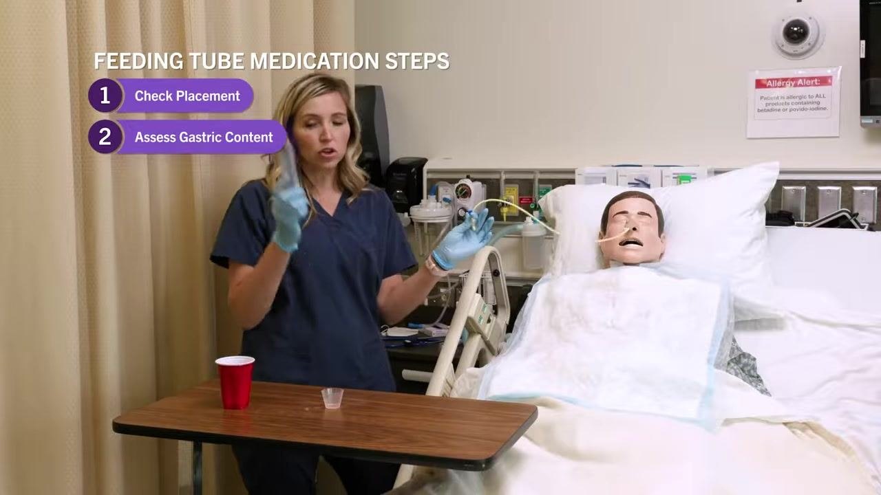 Nurse demonstrating clamping the tube with gloved hands beside a patient mannequin in a hospital bed, with on-screen steps 1 and 2 displayed.