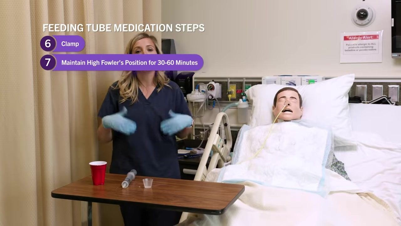 Nurse clamping the feeding tube, with on-screen text highlighting step 6: "Clamp." Supplies on the table, mannequin in bed.