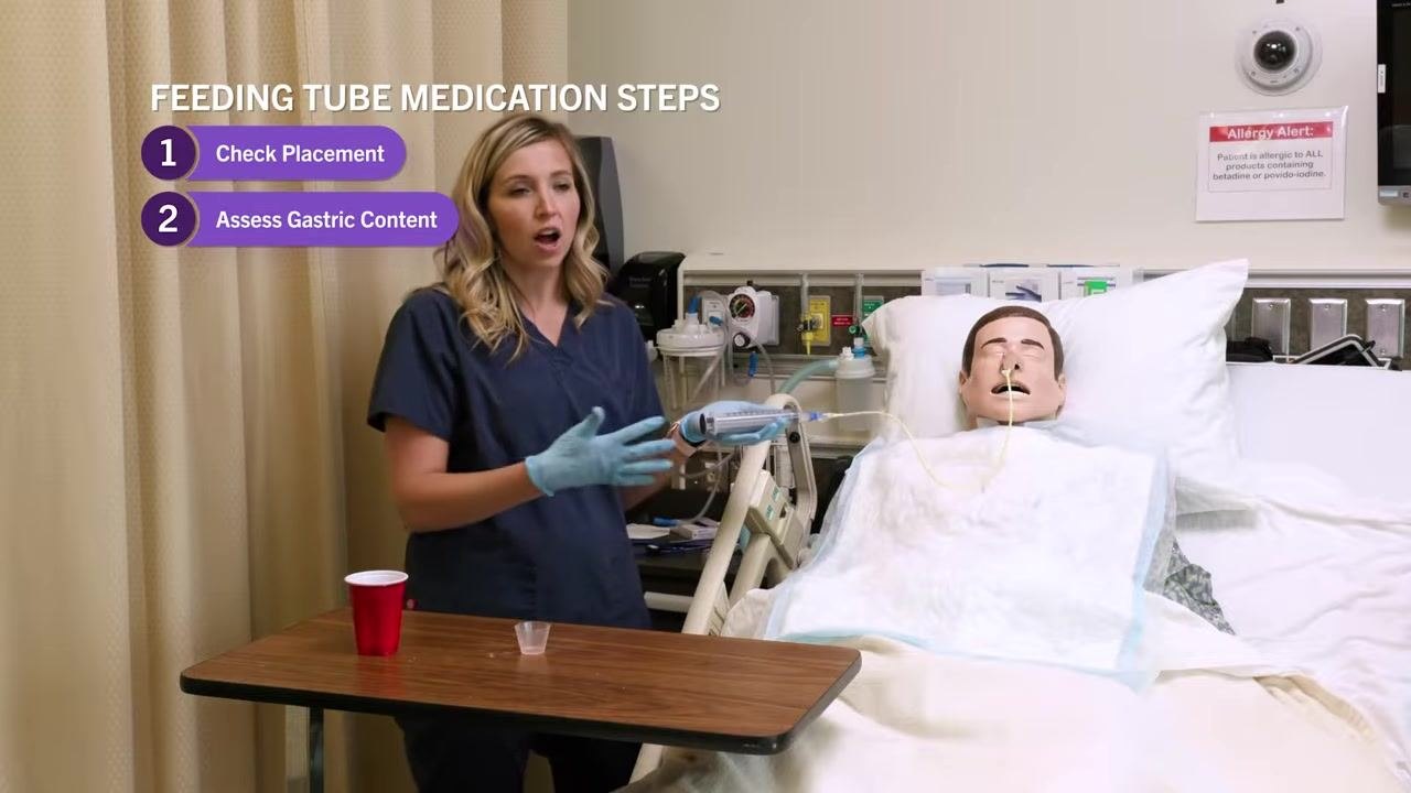 Nurse holding the syringe while emphasizing the importance of returning gastric content, with on-screen text "Feeding Tube Medication Steps: 1. Check Placement, 2. Assess Gastric Content."