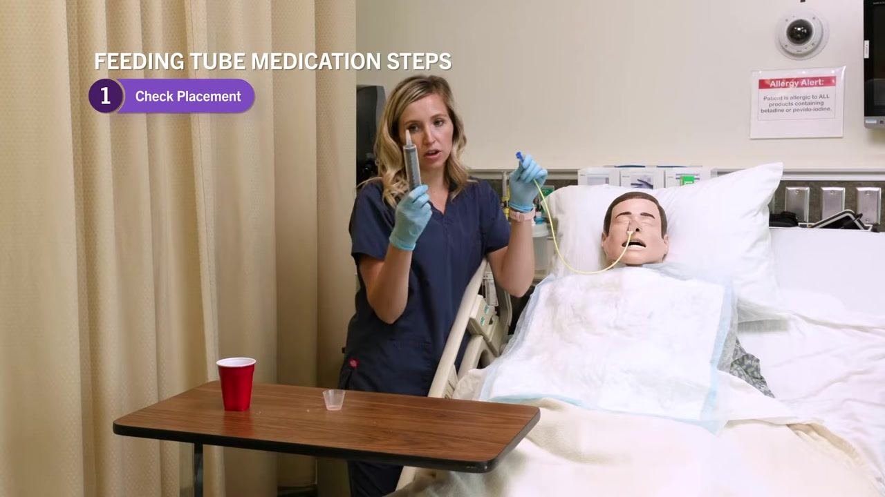 Nurse holding up the NG tube and 60 mL syringe, demonstrating the aspiration process, with on-screen text "Feeding Tube Medication Steps: 1. Check Placement."