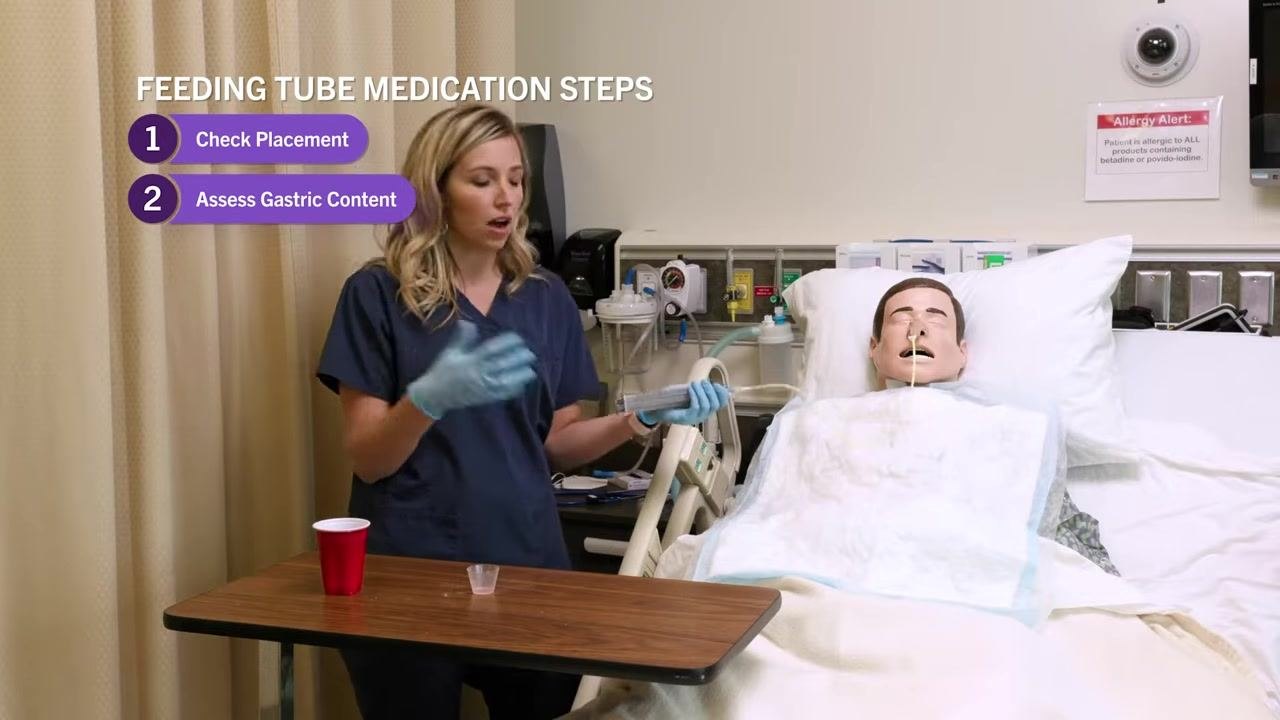 Nurse holding the syringe while explaining documentation and readiness, with on-screen text "Feeding Tube Medication Steps: 1. Check Placement, 2. Assess Gastric Content."
