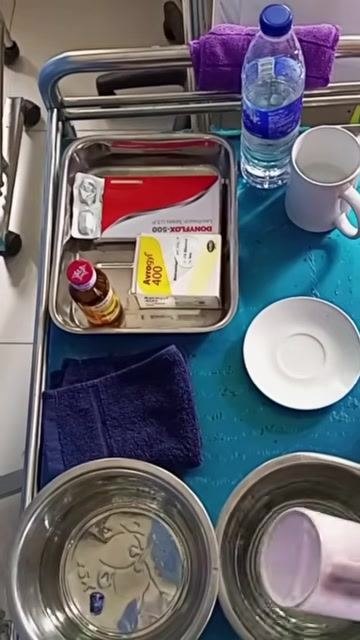 A medical tray organized with medication boxes, a bottle of water, two cups, a saucer, a towel, and two bowls of water, ready for medication administration.