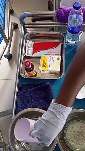A gloved hand rinsing a cup in a bowl of clean water on the medical tray.