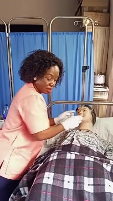 A healthcare worker assisting the patient in drinking the syrup by holding the saucer to their mouth.