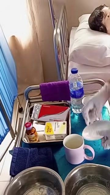 A gloved hand placing a clean saucer back on the tray, which holds a water bottle, medication bottle, boxes, cups, and towels.