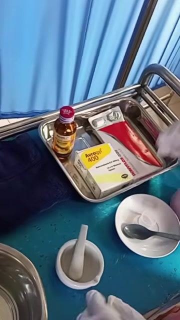 A gloved hand putting on a second glove at the medication preparation area, with a kidney dish and other supplies visible nearby.