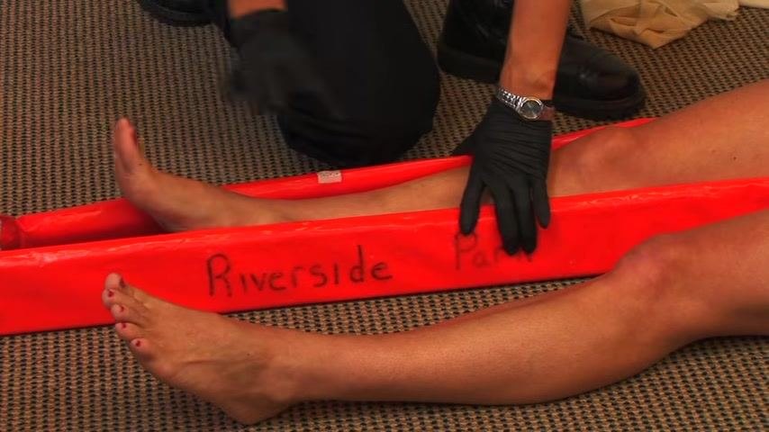 A responder begins wrapping a cravat above the knee to secure the splint, ensuring the knot rests on the rigid side.