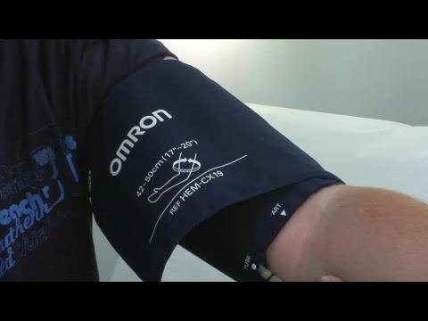 Close-up of an arm wearing an OMRON blood pressure cuff, showing the size range (17–23 cm) and model number (HEM-CX19) properly positioned on the upper arm.