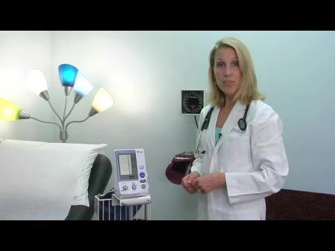 A doctor stands next to a blood pressure monitor, emphasizing the importance of device quality and proper fit in a well-lit clinical exam room.