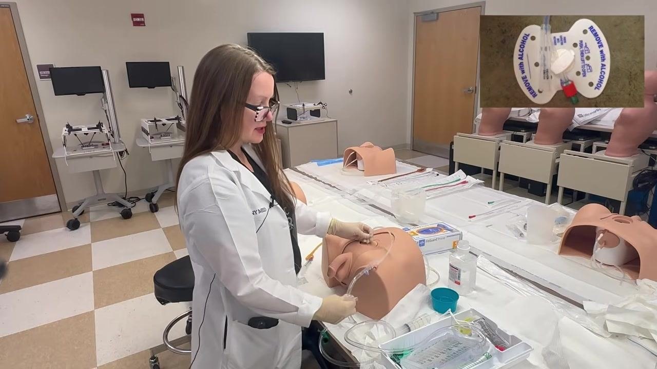 Securing the suprapubic catheter with a securement device on a training model, with a close-up inset showing the device labeled "REMOVE WITH ALCOHOL" and the tubing snapped in place