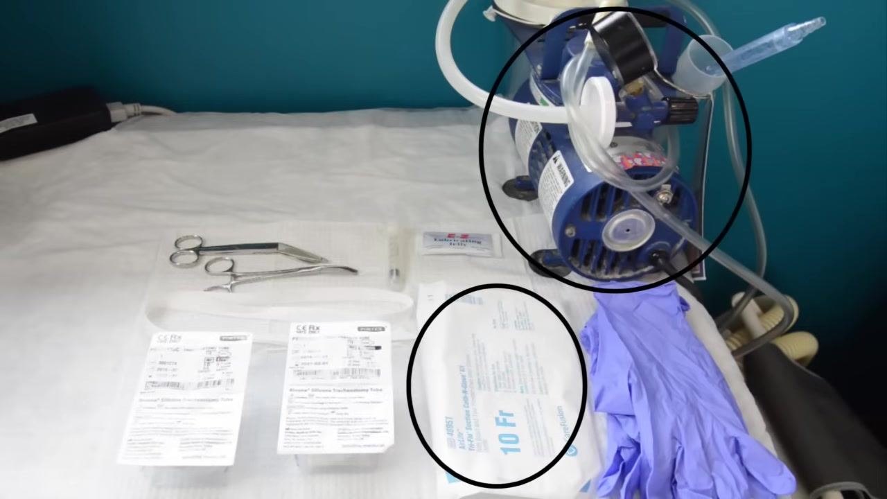 A gloved caregiver holding a trach tube and inflating the cuff with a syringe to check for proper inflation.