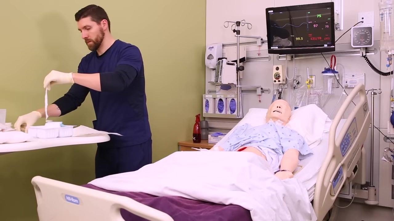 Nurse using sterile forceps to pack saline-soaked gauze into the wound of a patient mannequin, close-up of wound area and hands