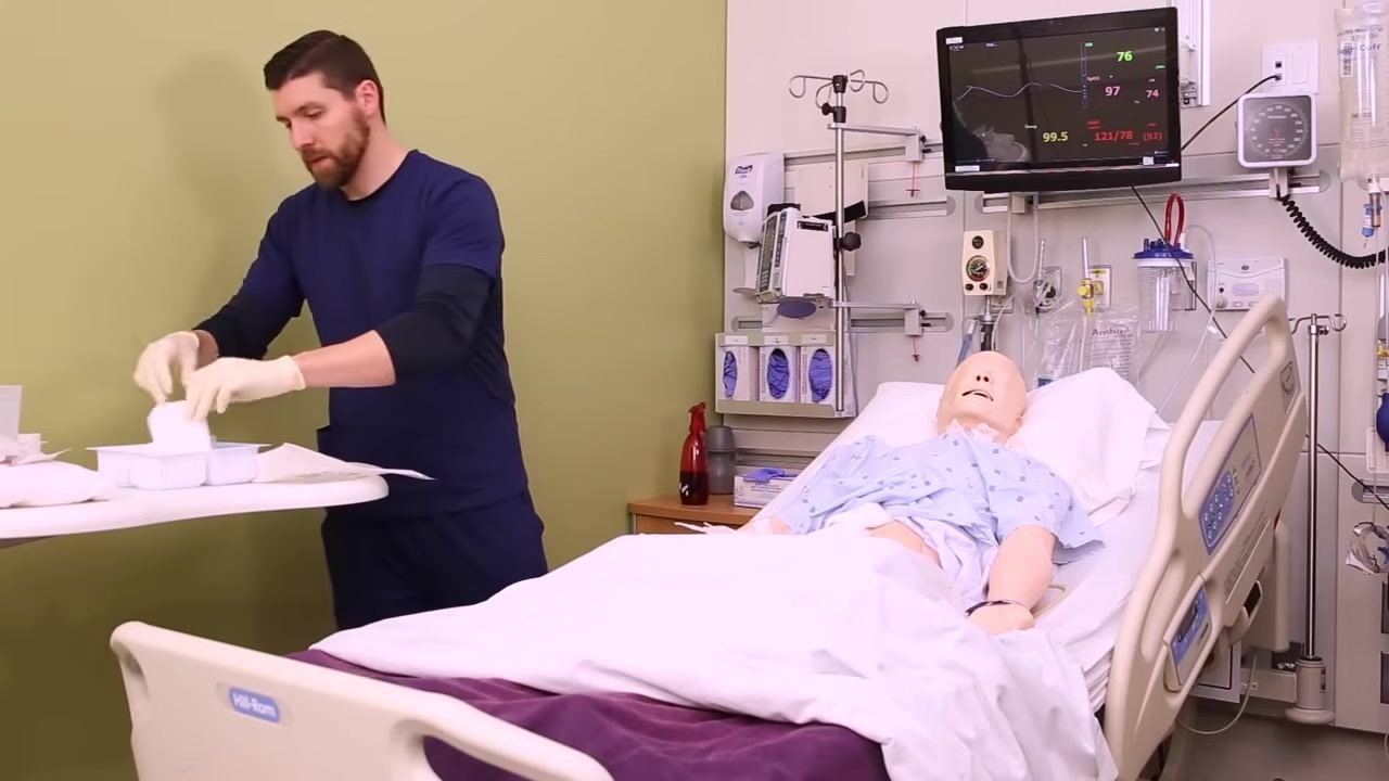 Nurse picking up an ABD pad from the sterile tray, preparing to cover the wound on the patient mannequin