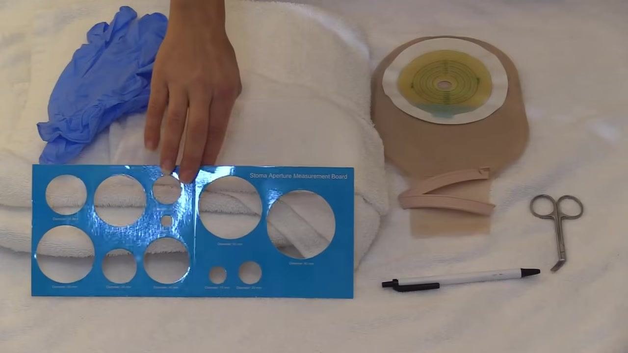 A hand pointing to the wafer on the pouch next to a stoma model, with all supplies ready for use