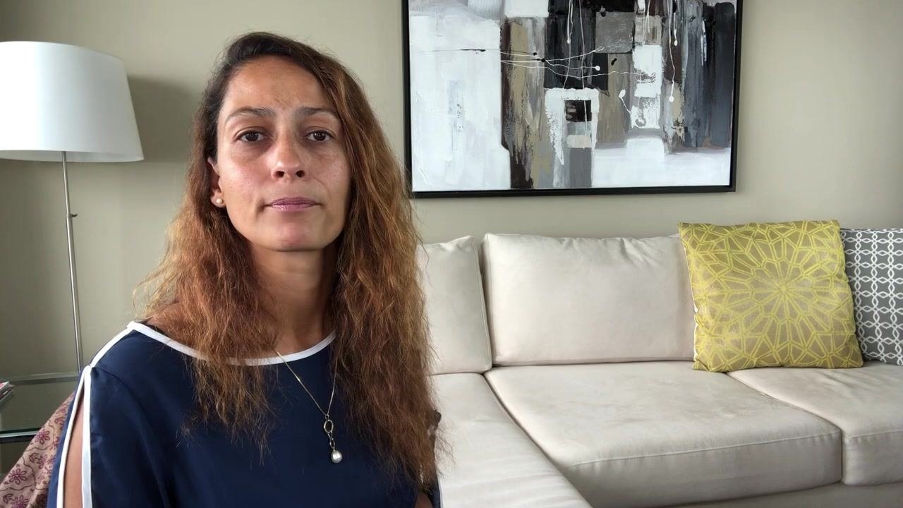 Presenter concluding the guide and summarizing the safe disposal process for needles and sharps, seated in a living room with a beige couch, yellow and gray pillows, a modern painting, and a white floor lamp.