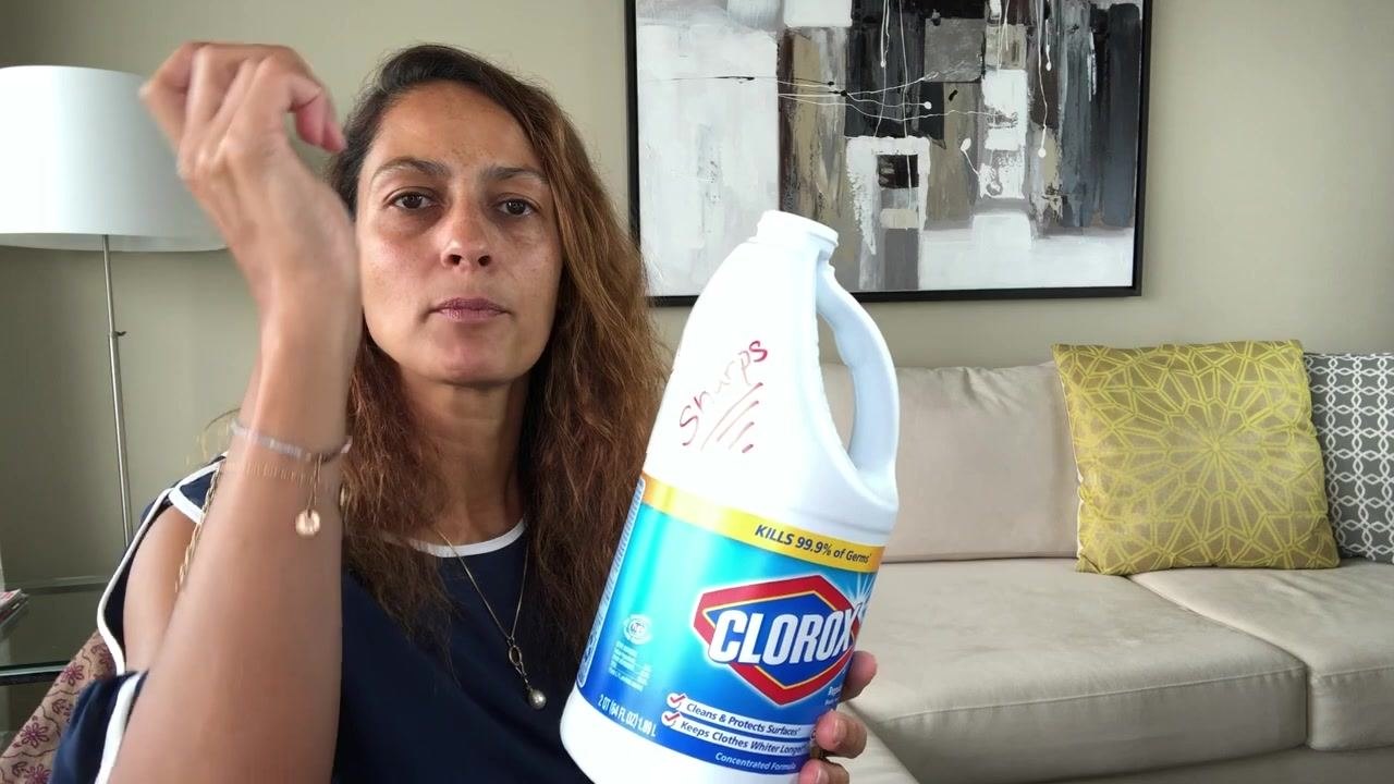 Person dropping a used sharp into the labeled bleach bottle, holding the container upright with the lid removed.