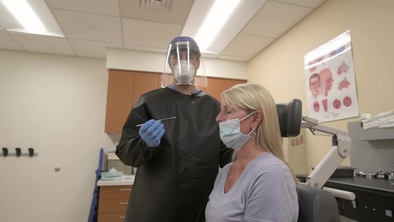 Clinician demonstrating swab insertion while the patient is seated, showing proper technique and readiness to manage patient interference.