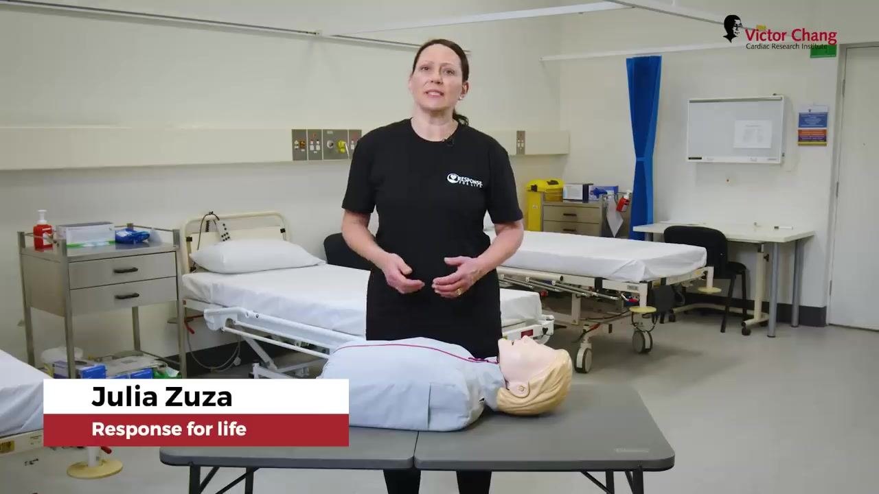 Instructor standing next to a manikin on a table in a clinical setting, with on-screen text "Step 2: Check for response."