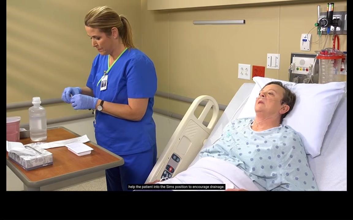 Nurse standing beside the bed, preparing to assist the patient who remains in a semi-upright position with a drape on the chest.