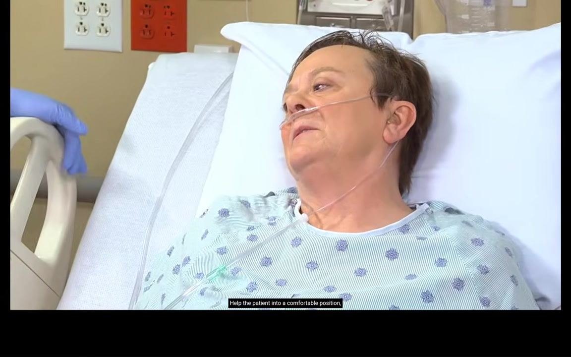 Nurse speaking to the patient at the bedside while holding the bed rail, preparing to assist with repositioning; the patient is alert and responsive.
