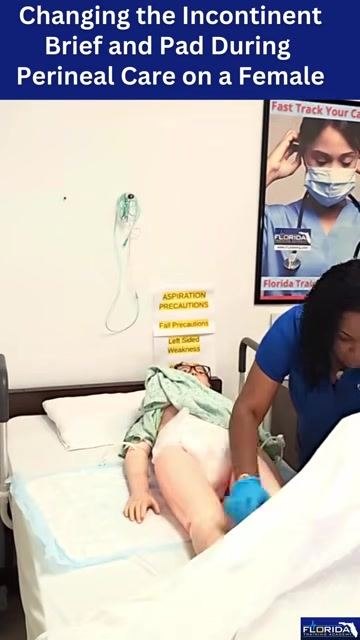 The caregiver repositions the mannequin's legs while ensuring the torso is properly aligned, with the mannequin lying on a hospital bed with a blue-backed pad underneath.