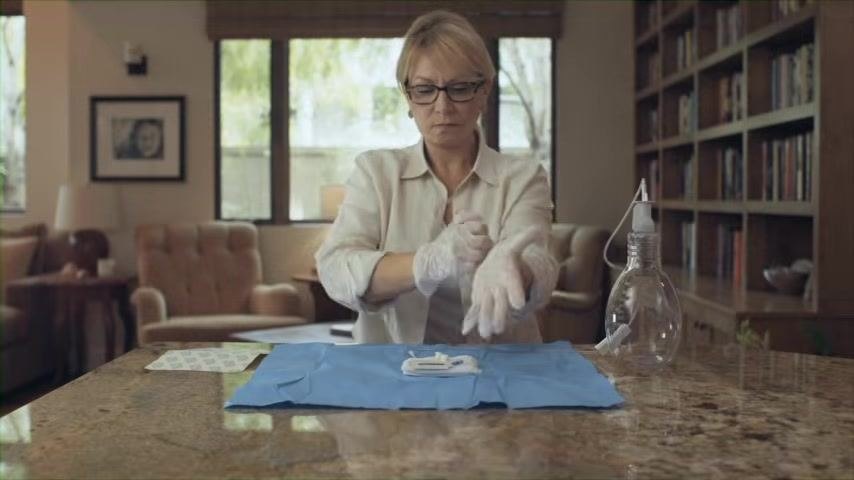 A gloved person working at a clean surface with medical supplies on a blue sterile drape.