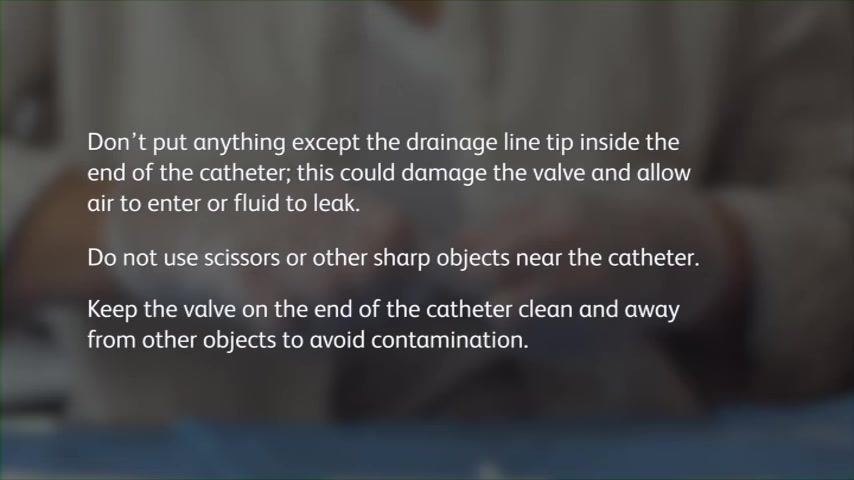 Close-up of gloved hands connecting the drainage line to the catheter on a blue sterile drape.
