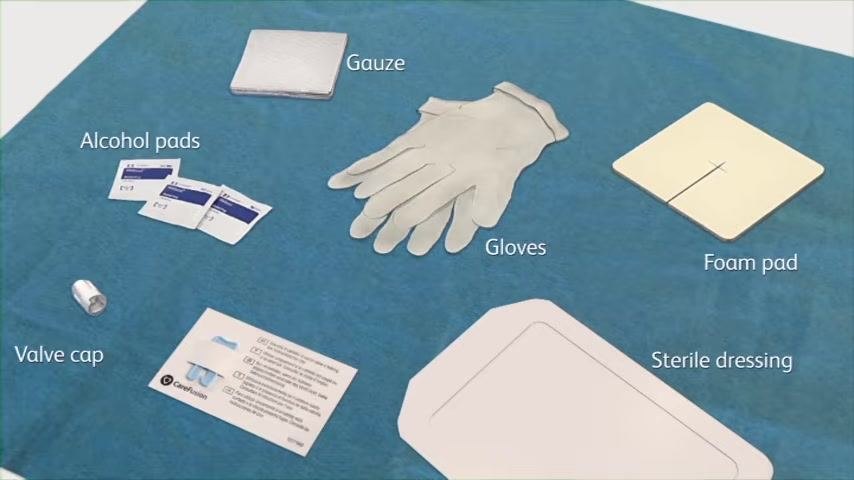 Contents of the PleurX drainage kit laid out on a blue sterile field: gloves, alcohol pads, gauze, foam pad, valve cap, sterile dressing, and an instruction card.