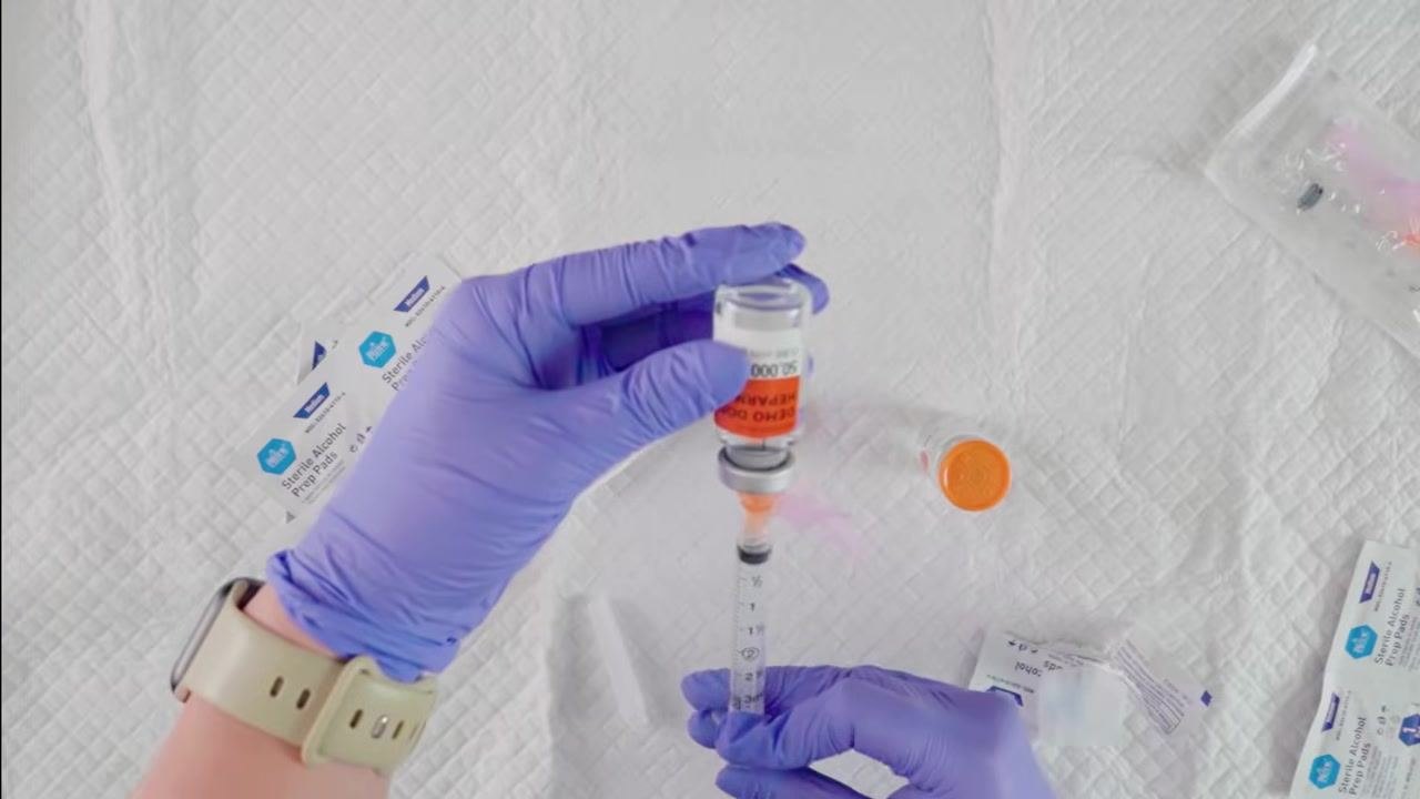 Gloved hands preparing supplies, including uncapping the needle and cleaning the vial