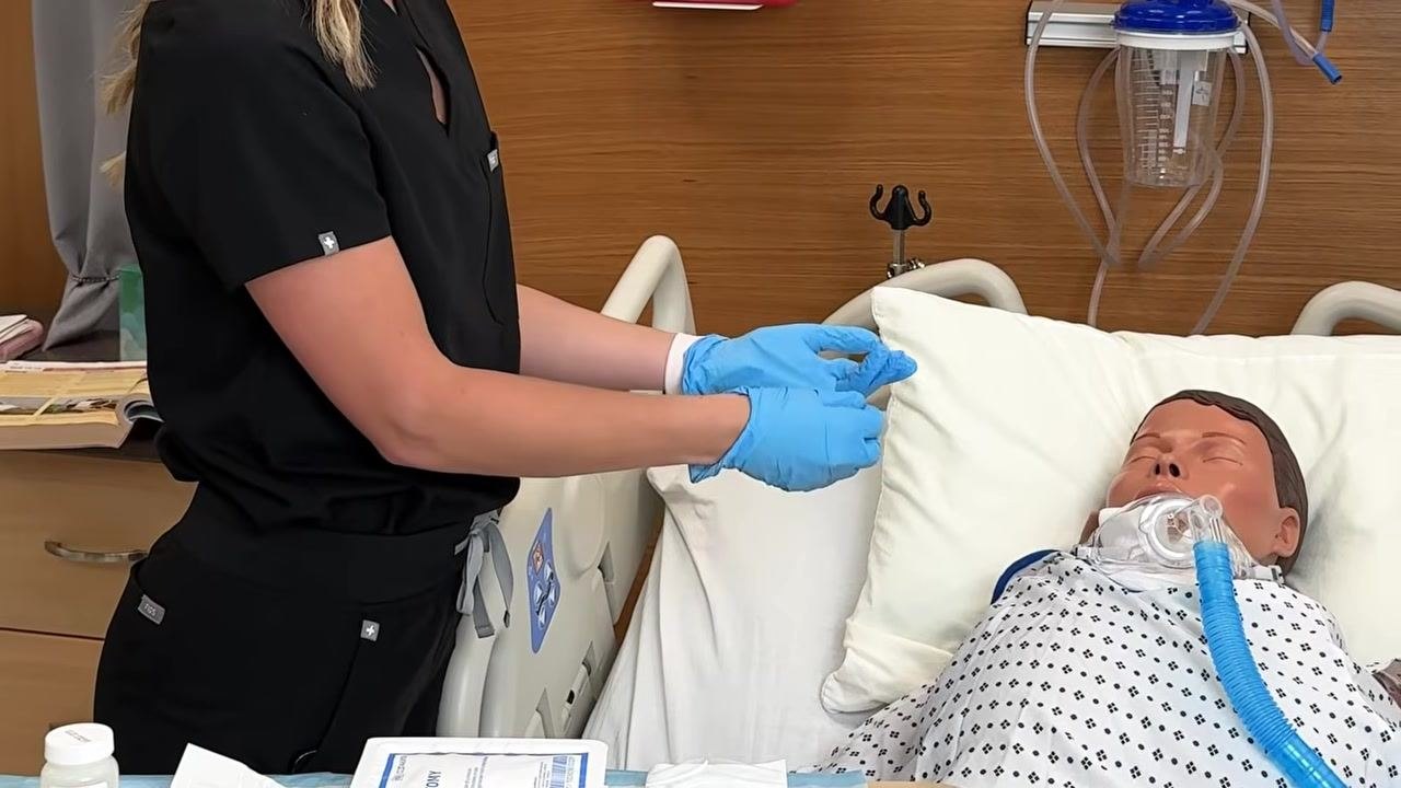 Healthcare provider wearing blue gloves, preparing to clean the injection site on a patient in a hospital bed