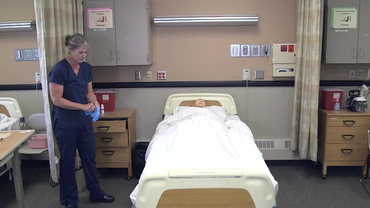 Nursing assistant putting on gloves with supplies visible on the bedside table