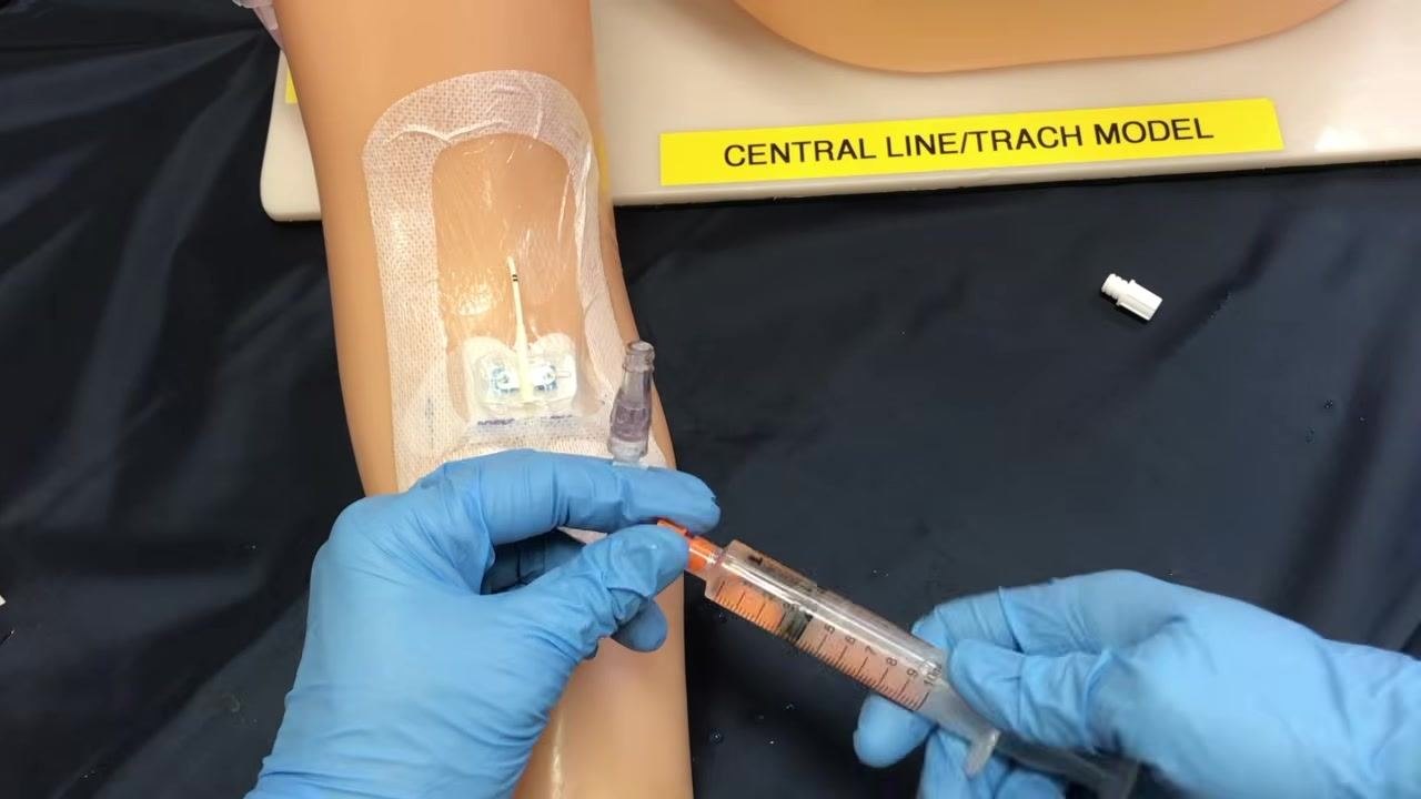 A gloved clinician attaching a syringe labeled CitraFlow 4% to the PICC line extension set while maintaining sterile technique