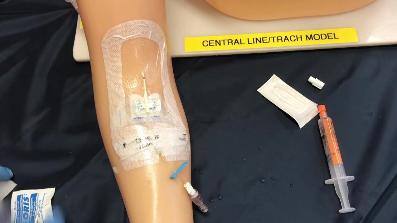 A gloved clinician disinfecting the PICC line access cap with an alcohol swab