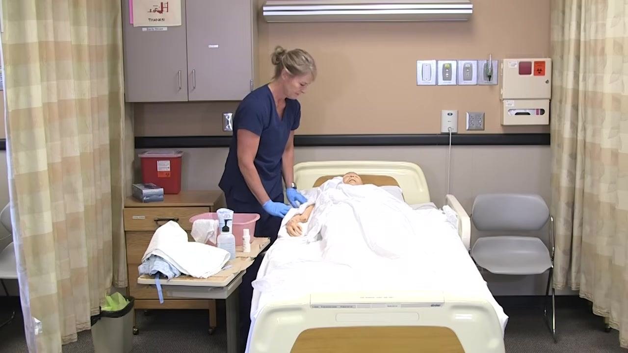 Nurse in blue scrubs covering the mannequin patient with linens after completing care for the upper body.