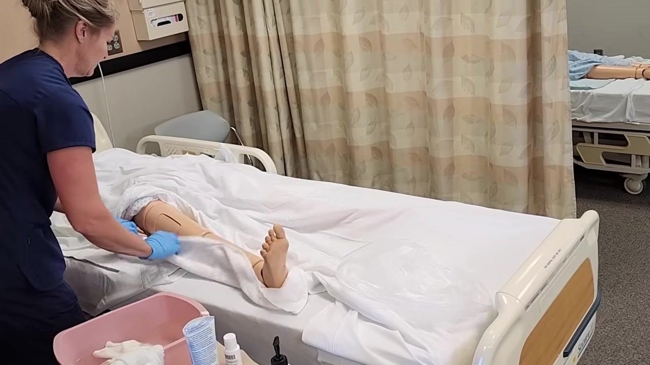 The healthcare worker is carefully drying the mannequin's foot, emphasizing the importance of dryness for diabetic residents.