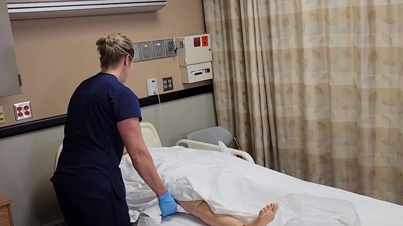 The healthcare worker is putting on fresh gloves, standing beside the bed and preparing for the next step.