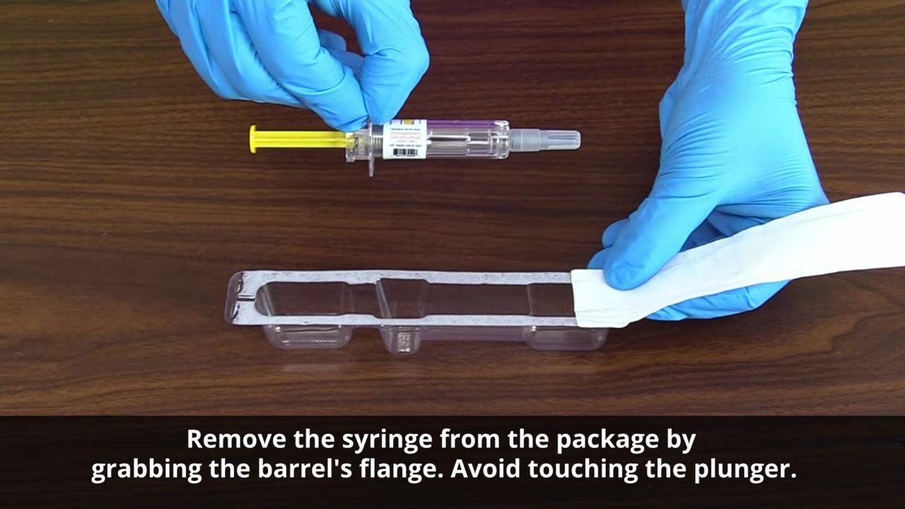 Gloved hands removing the syringe from its package by holding the barrel's flange without touching the plunger.