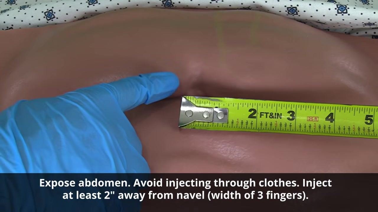 Gloved hand pointing to an exposed abdomen, indicating the injection zone at least 2 inches from the navel.