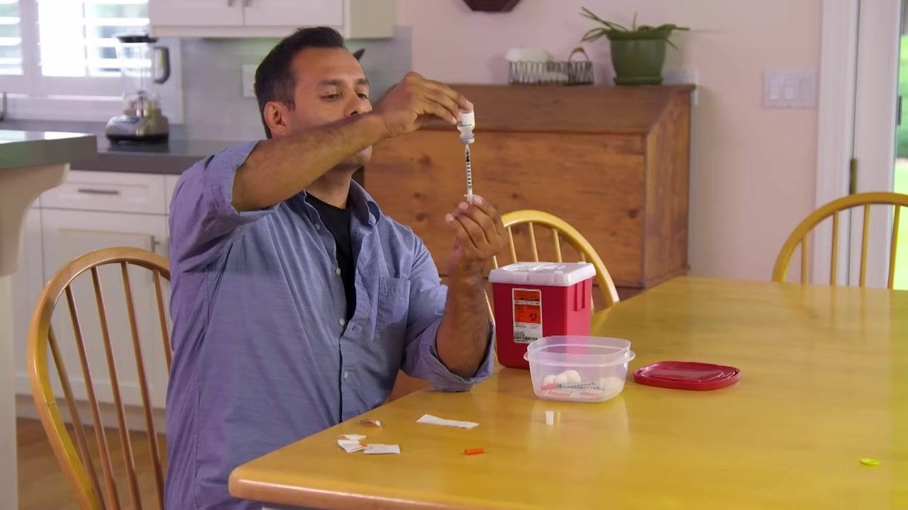 A person drawing medication into a syringe from an inverted vial, keeping the needle below the liquid surface.