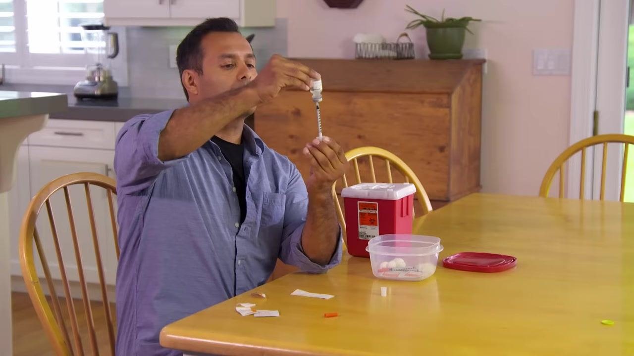 A person holding a vial upside down with a syringe inserted, pushing the plunger to inject air into the vial.