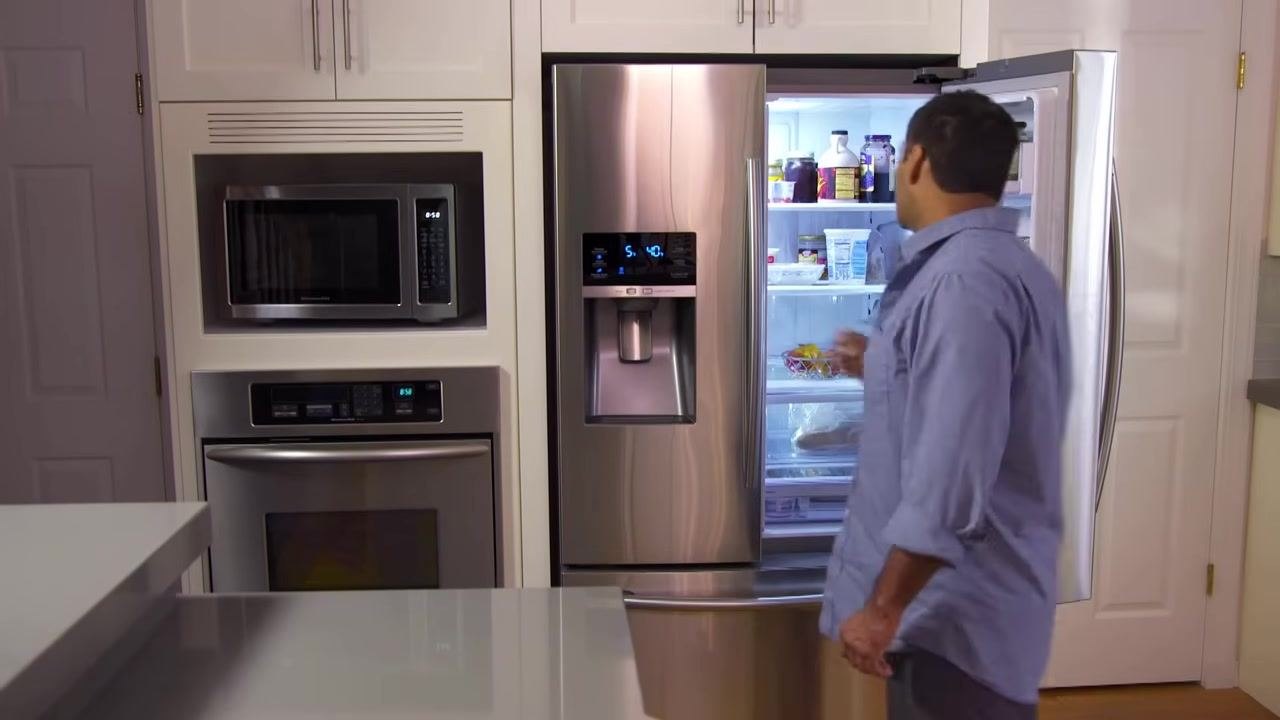 A person reaching into an open refrigerator in a kitchen, with various bottles and containers visible inside.