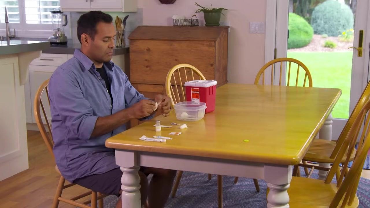 A person exposing their upper thigh at a kitchen table, with injection supplies laid out and ready.