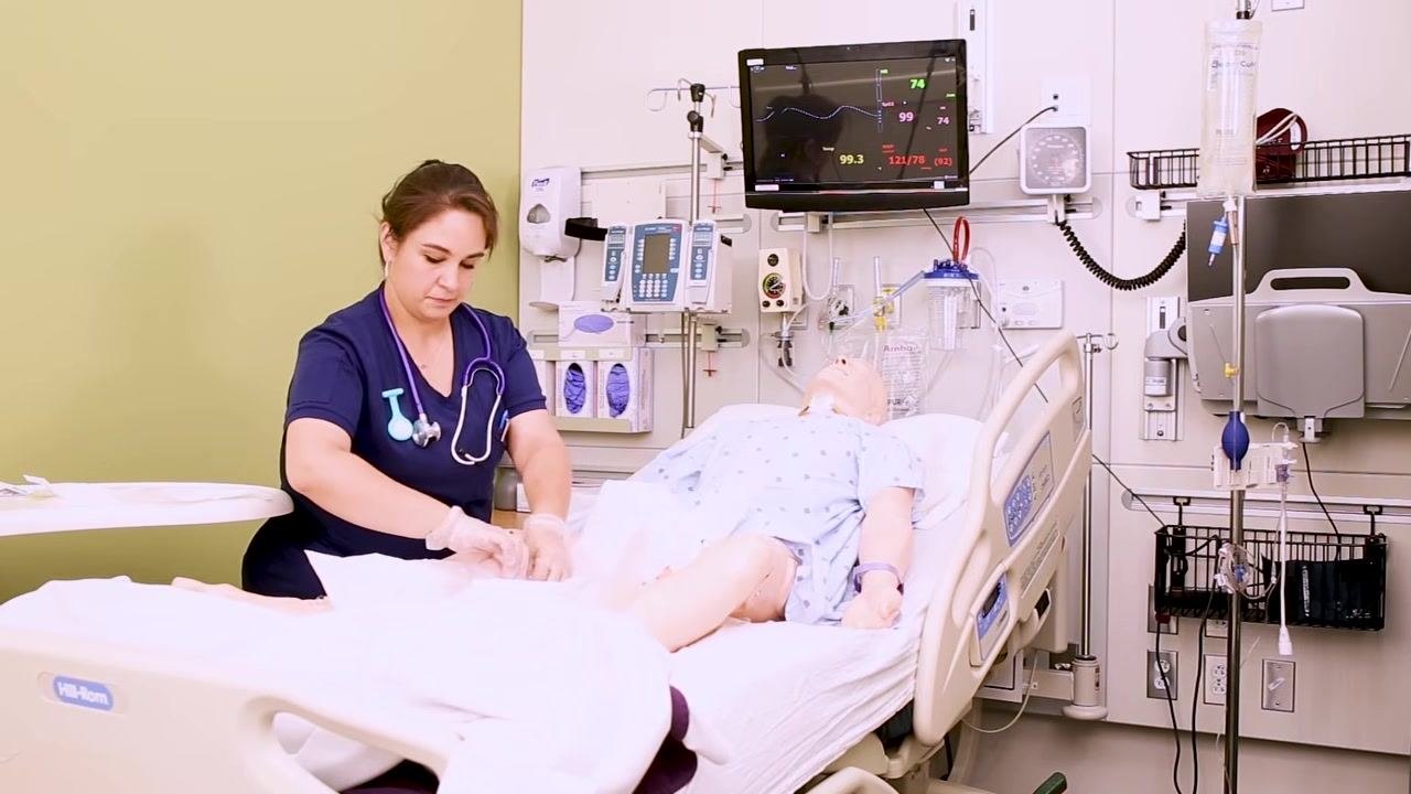 A nurse lubricates the Foley catheter by inserting it into the lubrication package, then sets it down on the sterile tray.