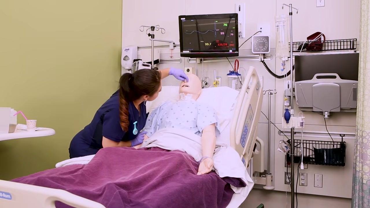 Nurse assessing the nasal patency of a patient mannequin in a hospital bed, with medical monitors and equipment visible in the background